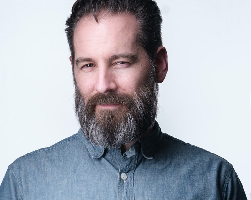 Business headshot of a man in a blue button-up shirt, with a medium-length beard.