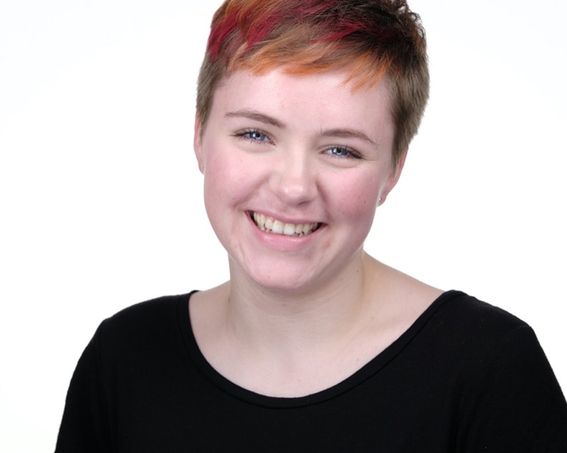 A young woman with short red and orange hair laughs towards the camera.