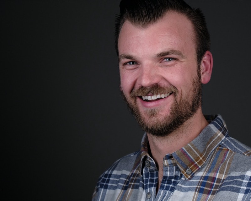 A man in a plaid shirt with a short dark beard smiling at the camera.