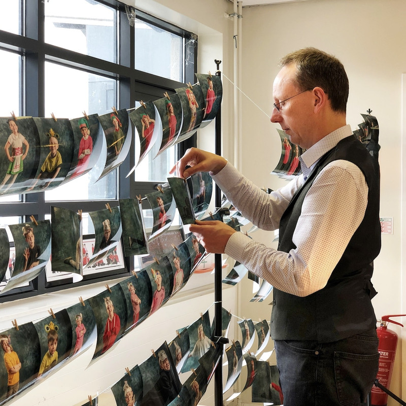 A man in a formal shirt and waistcoat is hanging printed photos onto a washing line for display.