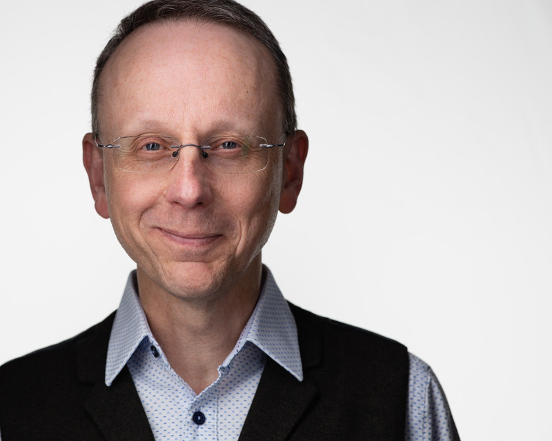 Richard is wearing a shirt with a dotted pattern, and a dark waistcoat. He smiles proudly at the camera.