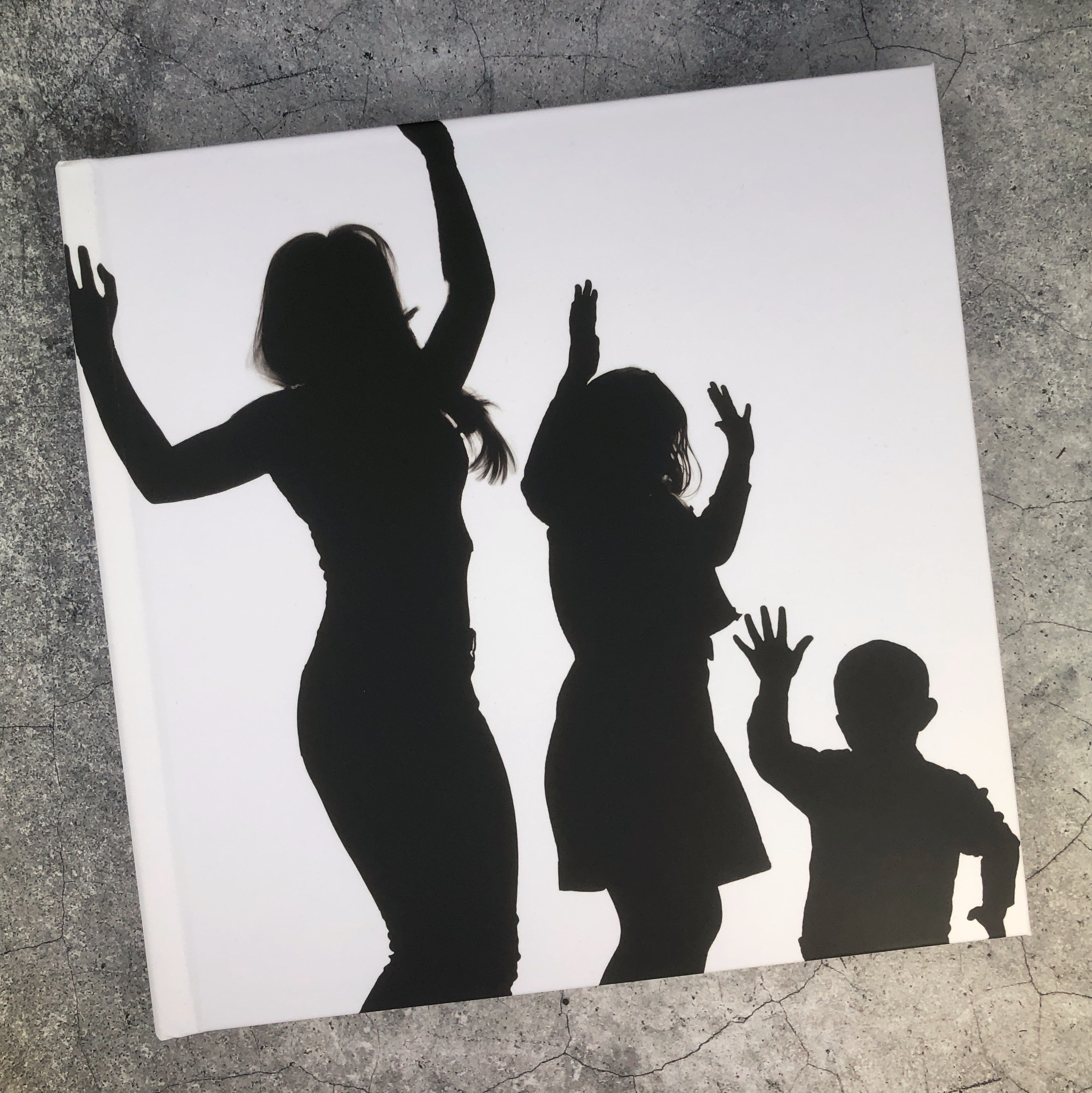 A white celebration book with silhouettes on the cover, sitting on a stone surface.