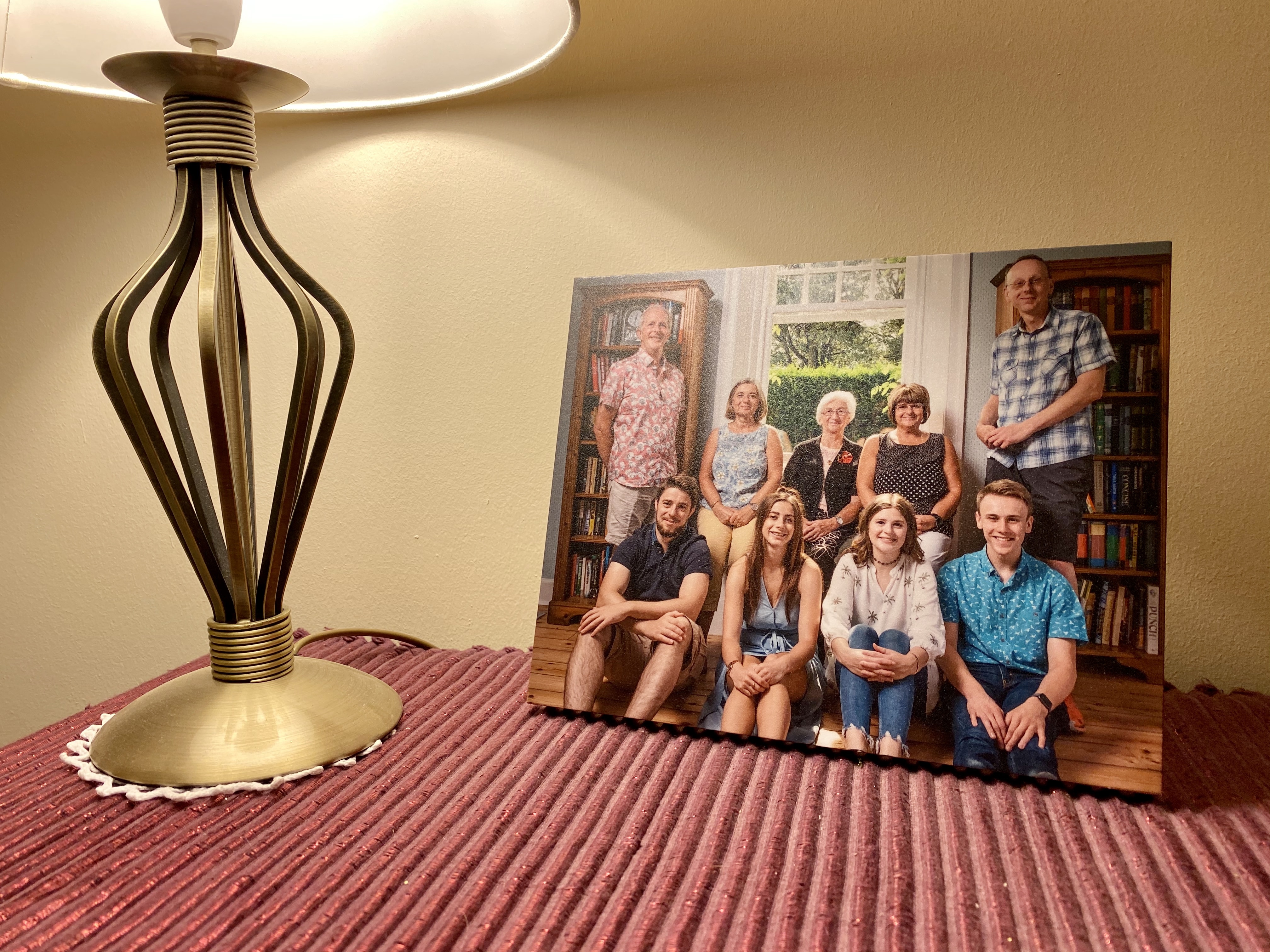 A family photo with two rows of people of differing ages, printed on a frameless panel and situated under a desk lamp.